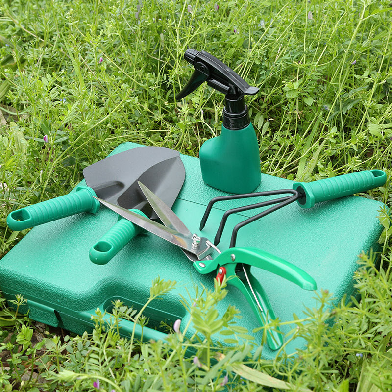 Set of gardening tools including a trowel, pruner, and sprayer on a green case in grass.