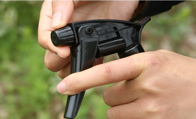 Black spray gun held by a person with a blurred green background