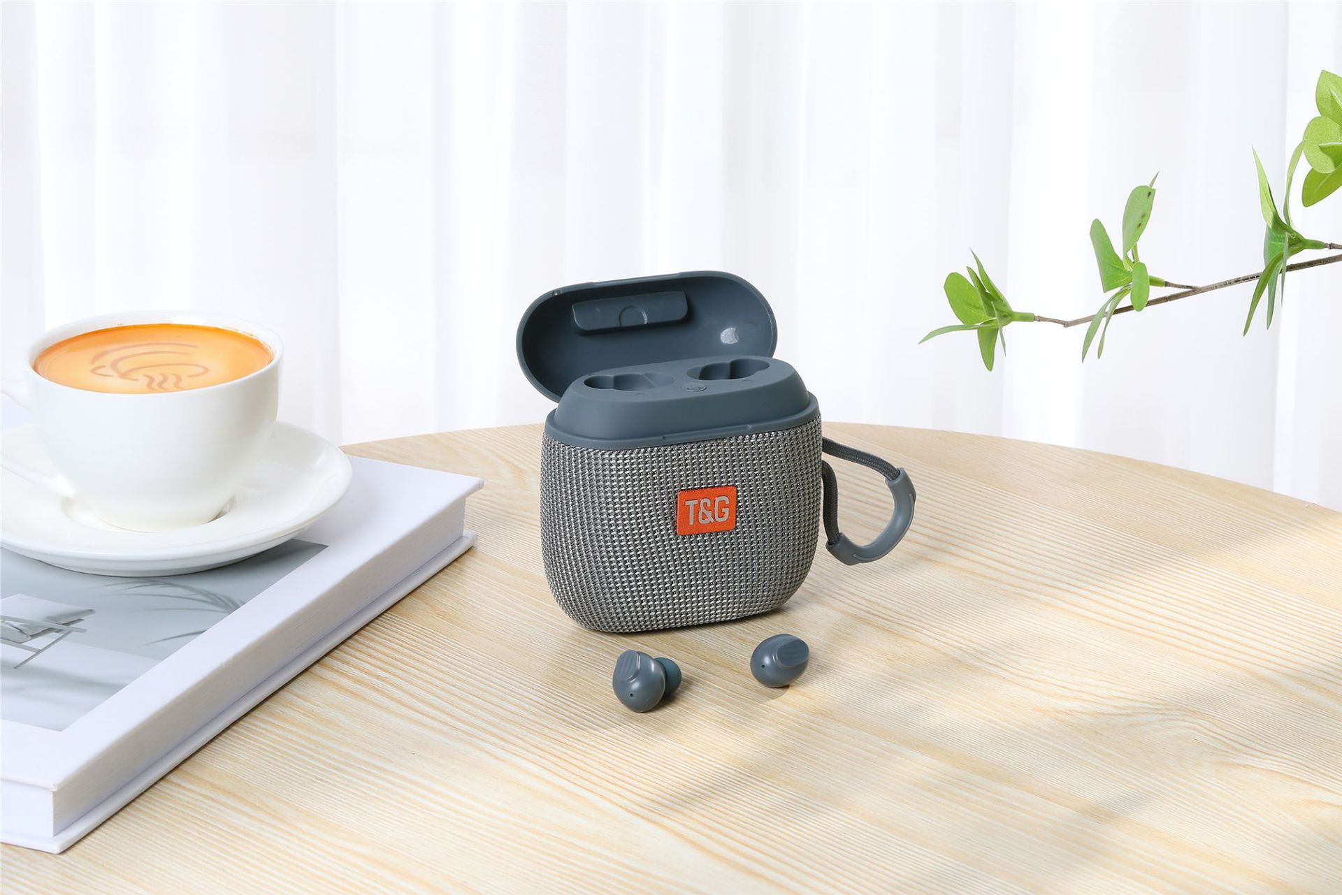 Gray TSG earbud case on a wooden table with a cup of coffee and book in the background