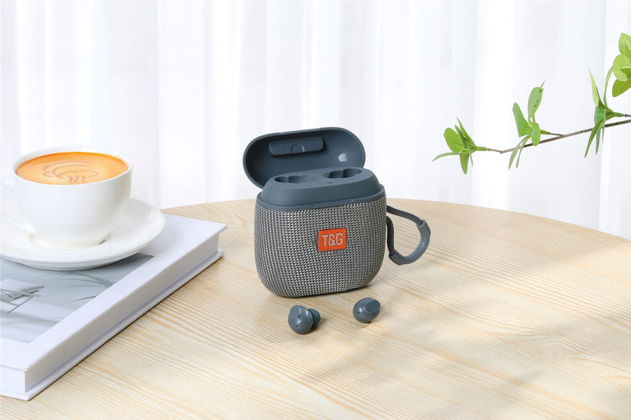Gray TSG earbud case on a wooden table with a cup of coffee and book in the background
