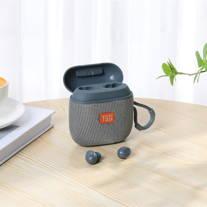 Gray wireless earbuds in a mesh case on a wooden table with a white curtain background