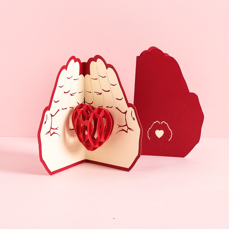 3D pop-up card with hands holding a heart on a pink background