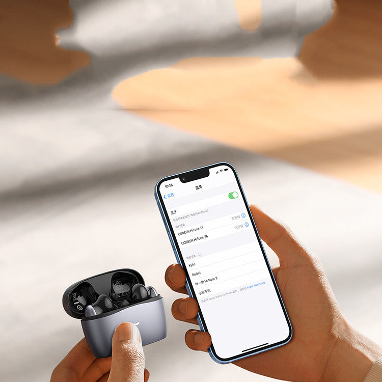 Person holding wireless earbuds and a smartphone with a blurred background