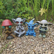 Four small figurines with unique designs on a pebble surface with greenery in the background