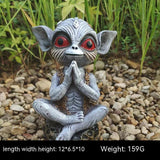 Statue of a creature with red eyes sitting on pebbles with plants in the background