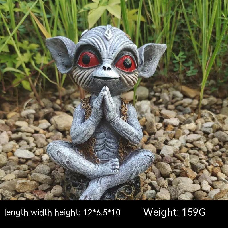 Statue of a creature with red eyes sitting on pebbles with plants in the background