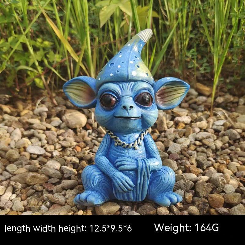 Blue creature figurine with a cone hat on pebbles with plant background