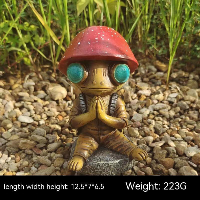 Small robot figurine with a red helmet and teal eyes sitting on a rock with grass in the background.