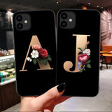 Two black phone cases with floral initials held in a hand against a blurred indoor background.