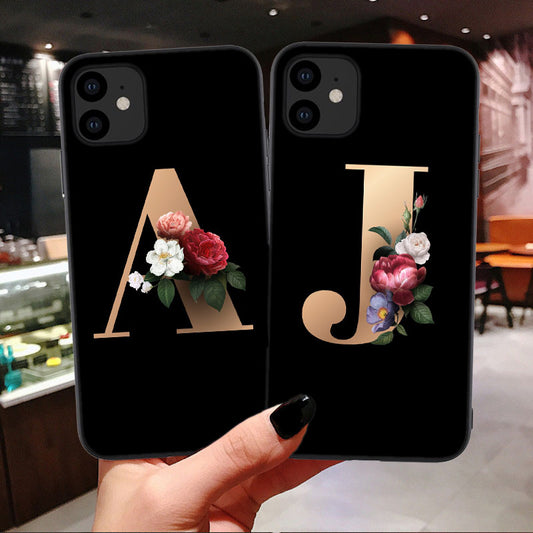 Two black phone cases with floral initials held in a hand against a blurred indoor background.