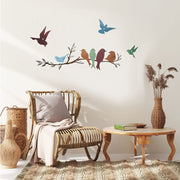 Decorative wall stickers of birds on a branch in a living room setting with a wicker chair and wooden table.