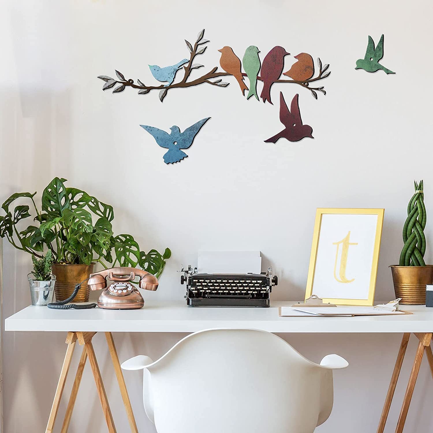Decorative wall art of birds on a branch above a desk with plants and a typewriter.