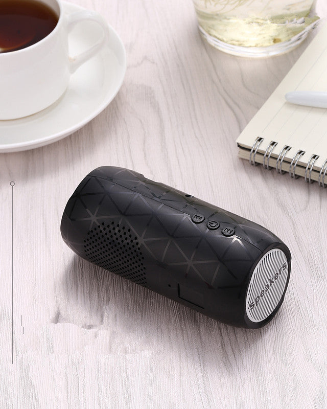 Black portable speaker on a light wooden surface with a cup of tea and notebook in the background.