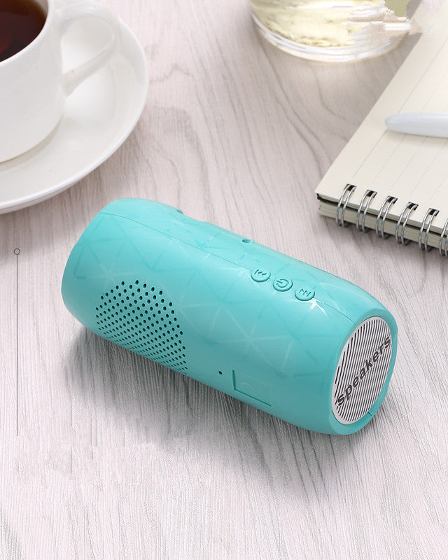 Turquoise Bluetooth speaker on a light wooden surface with a cup of tea and notebook in the background.