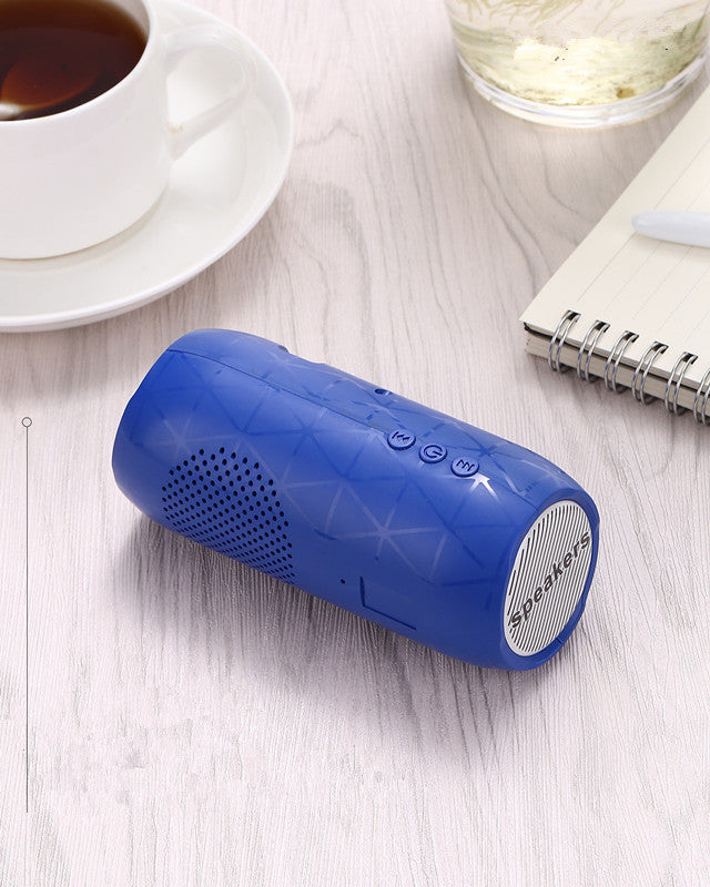 Blue portable speaker on a light wooden surface with a cup of tea and notebook in the background.