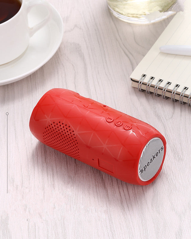 Red portable speaker on a light wooden surface with a cup of coffee and notebook in the background.