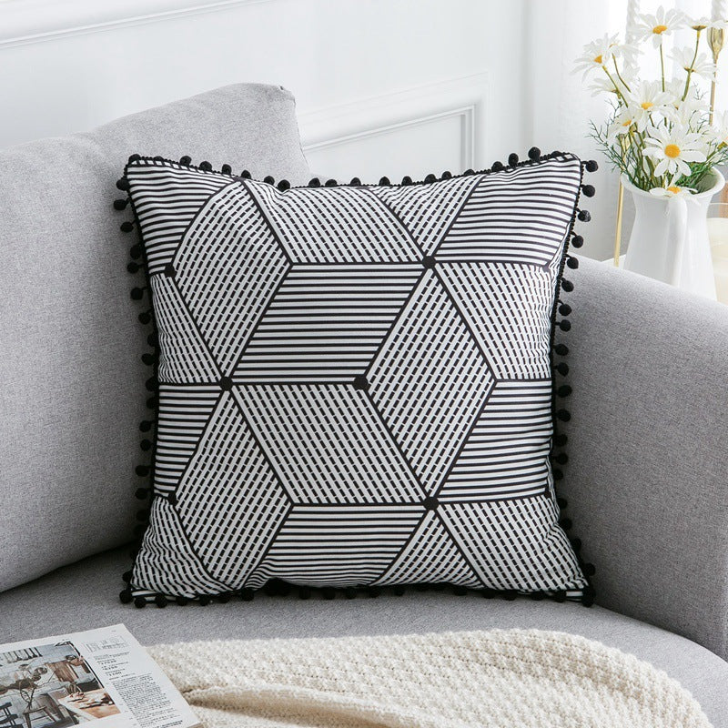 Geometric patterned pillow with pom-pom trim on a gray sofa