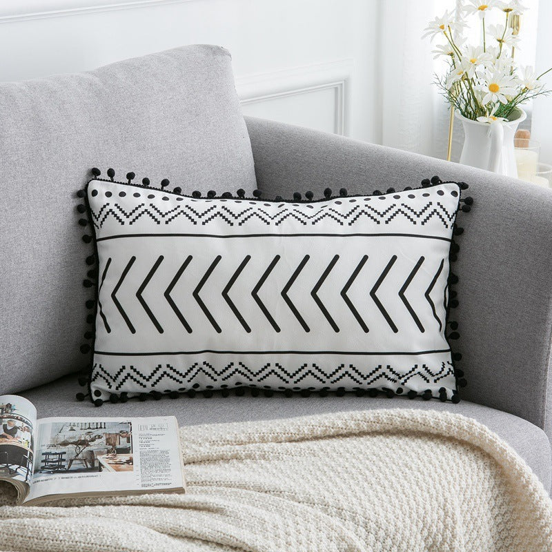 Decorative pillow with black and white pattern on a gray sofa with a blanket and magazine.
