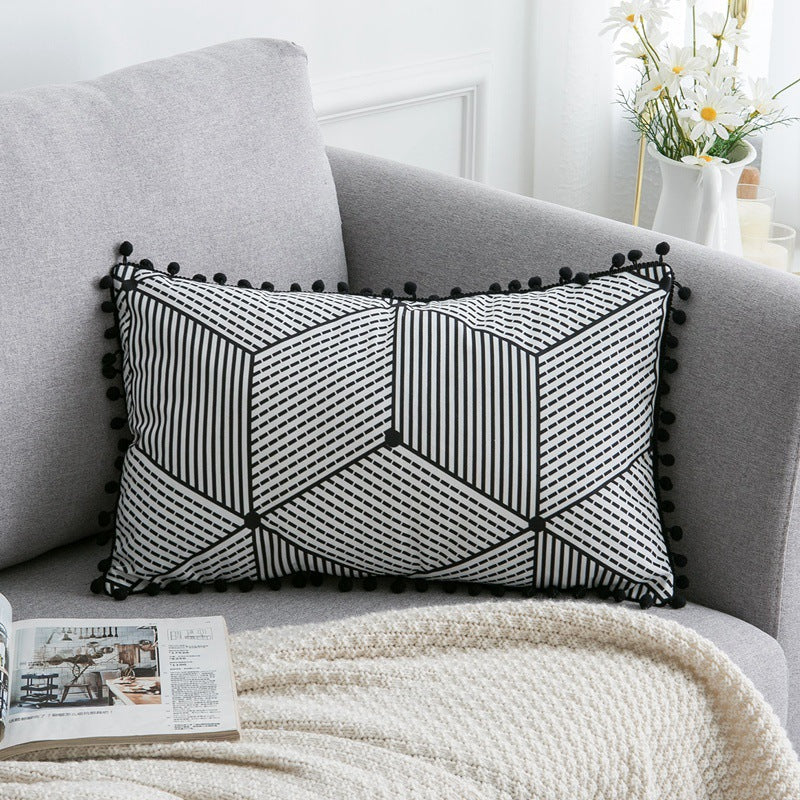 Decorative pillow with geometric pattern on a gray sofa with a magazine and blanket.