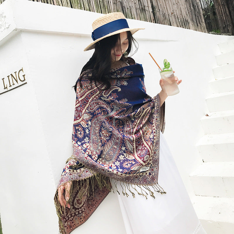 Woman wearing a patterned scarf and straw hat, holding a drink, with a white background.