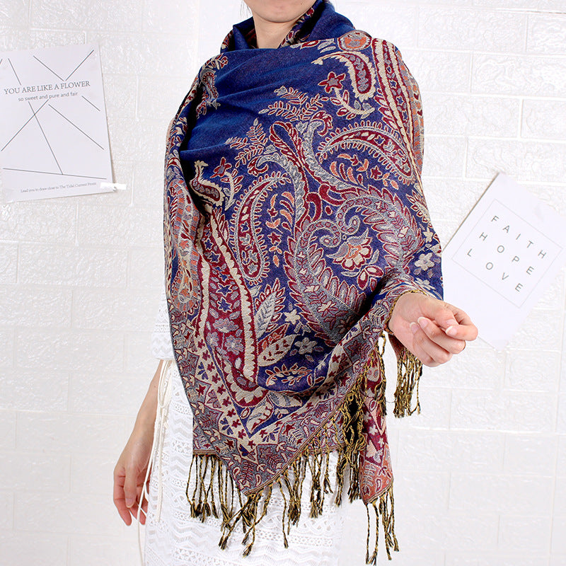 Person wearing a blue paisley patterned scarf with tassels on a white background