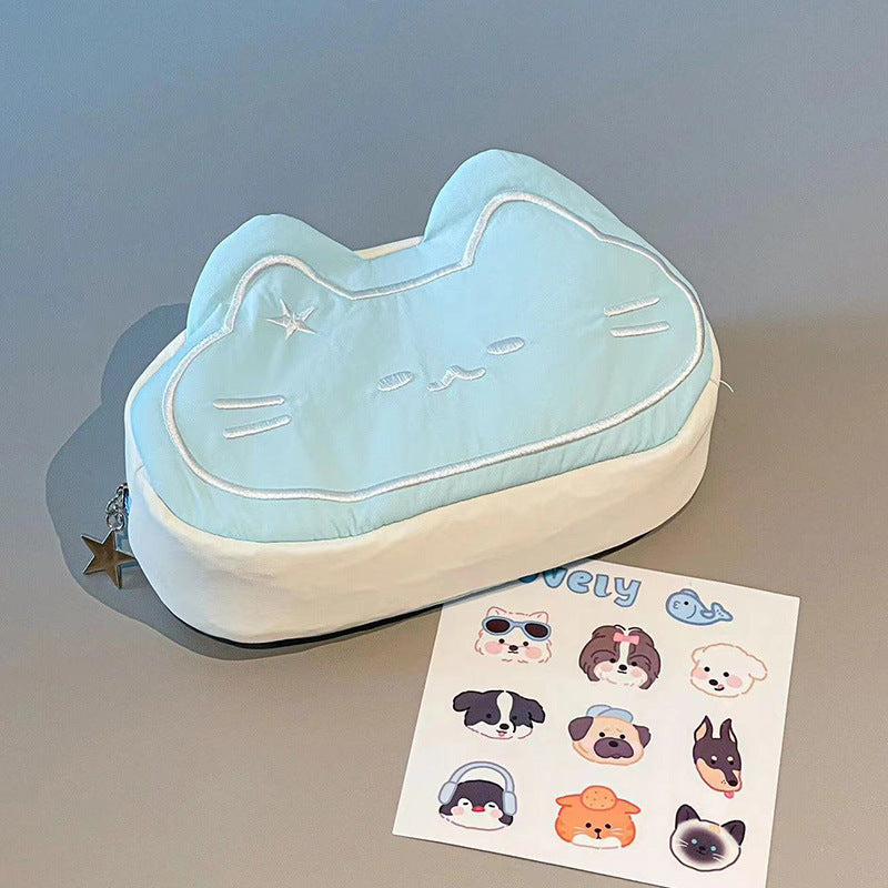 Light blue cat-shaped cushion with a star charm on a gray surface, next to a sheet of dog stickers.