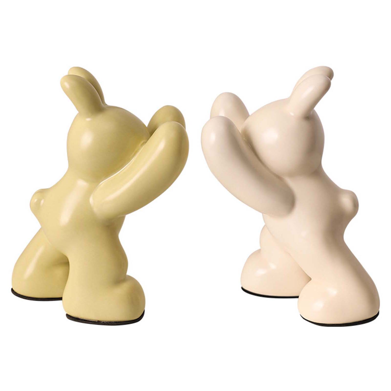 Two ceramic figures, one yellow and one beige, on a white background