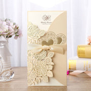 Decorative wedding invitation card with floral designs and a bow on a wooden surface.