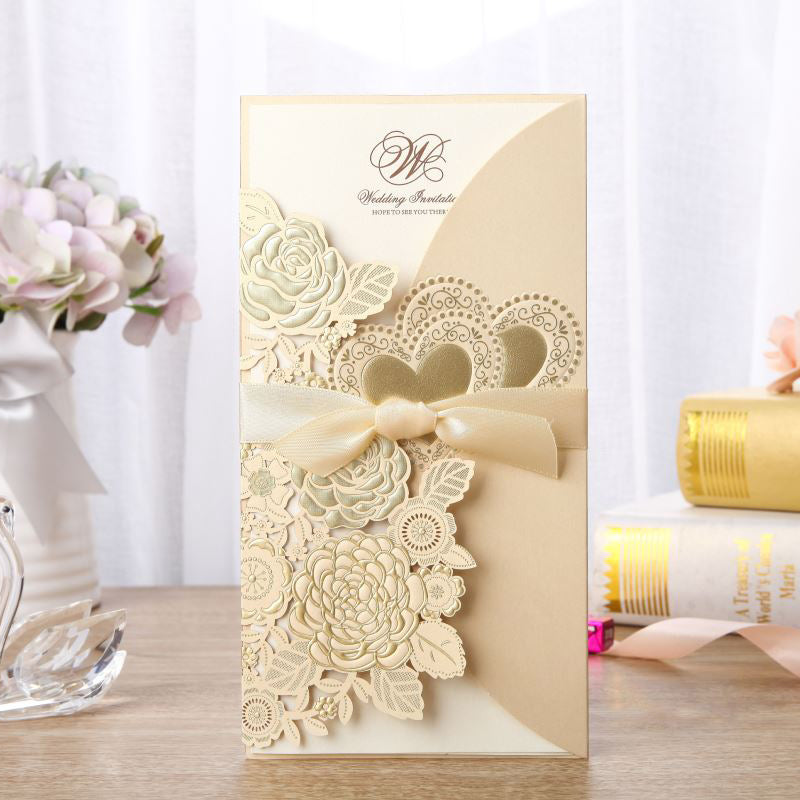 Decorative wedding invitation card with floral designs and a bow on a wooden surface.