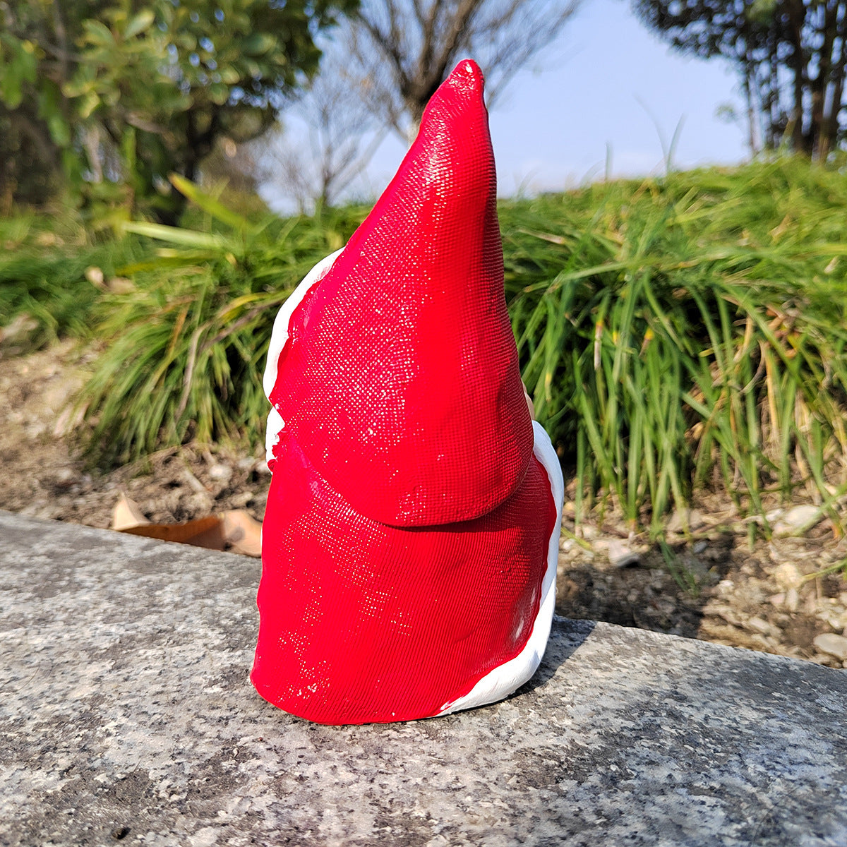 Red gnome figure on a stone surface with greenery in the background