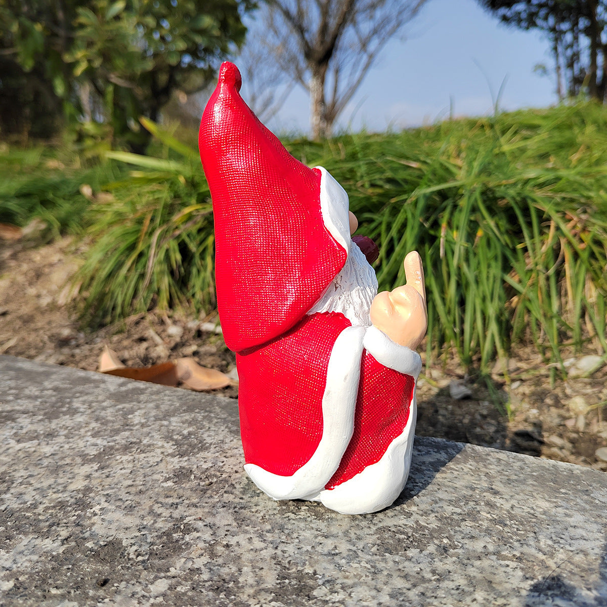 Gnome figurine with a red hat and white beard on a stone surface with greenery in the background