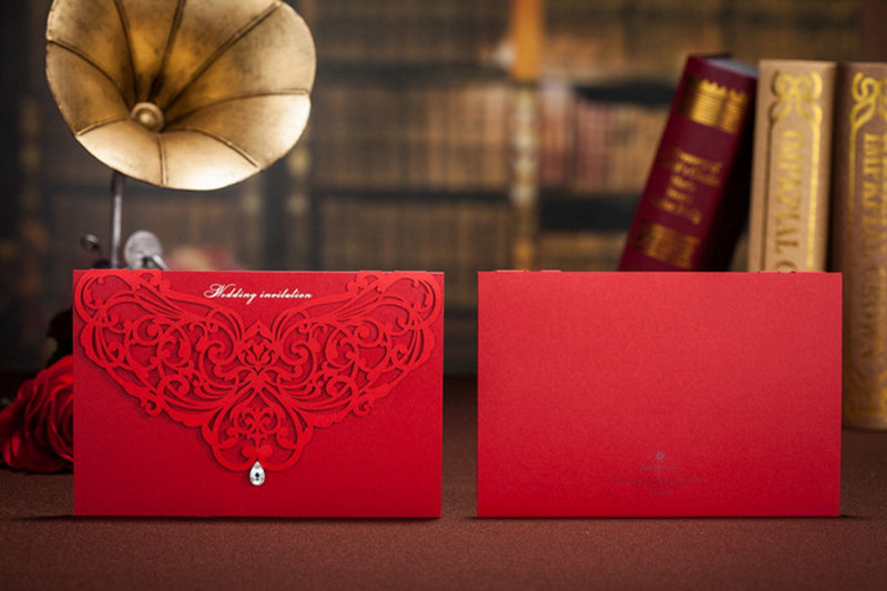 Two red envelopes with intricate designs on a wooden surface with books and a vintage lamp in the background.