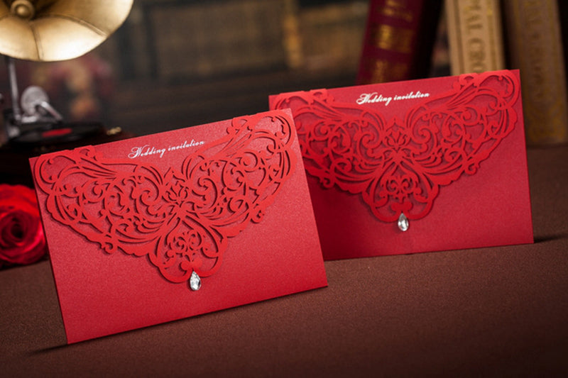 Two red wedding invitations with intricate designs on a dark surface.