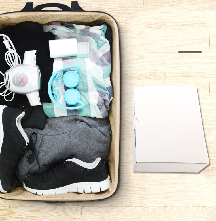 Open suitcase with clothes and electronic items on a wooden surface