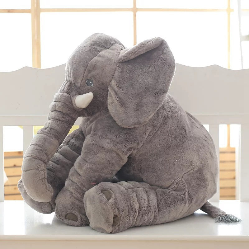 Gray plush elephant toy on a white surface with a light wooden background