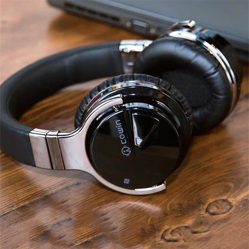 Black and silver headphones on a wooden surface with a laptop in the background