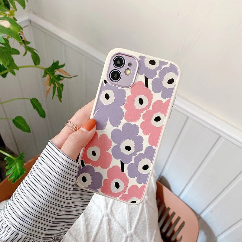 Phone case with floral pattern held by a person against a light-colored wall.