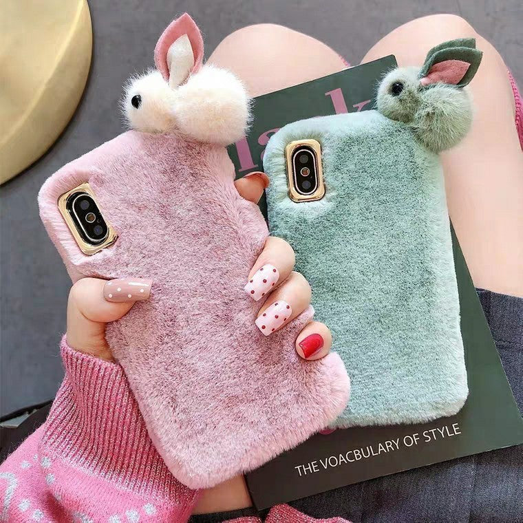 Two fluffy phone cases, one pink and one green, held by a person with a magazine underneath.