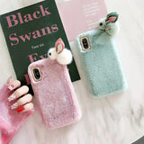 Two fluffy phone cases, one pink and one green, with rabbit ears on a white surface.