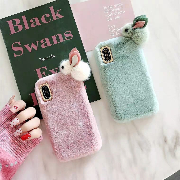Two fluffy phone cases, one pink and one green, with rabbit ears on a white surface.