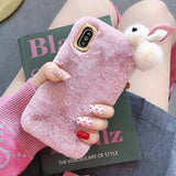 Pink fluffy phone case with a bunny charm held by a person on a magazine