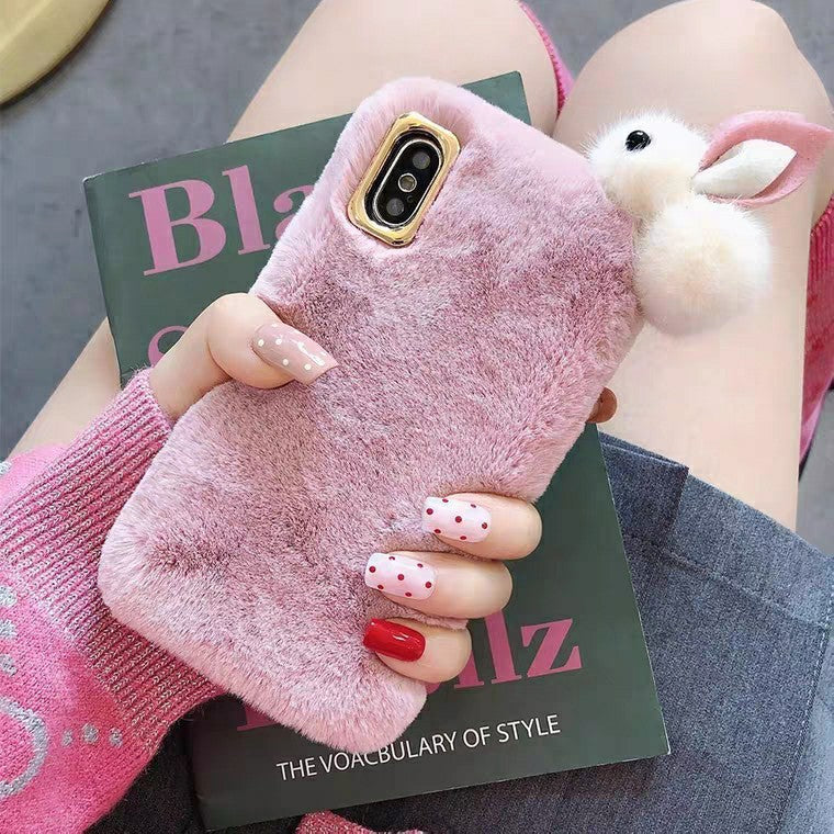 Pink fluffy phone case with a bunny charm held by a person on a magazine