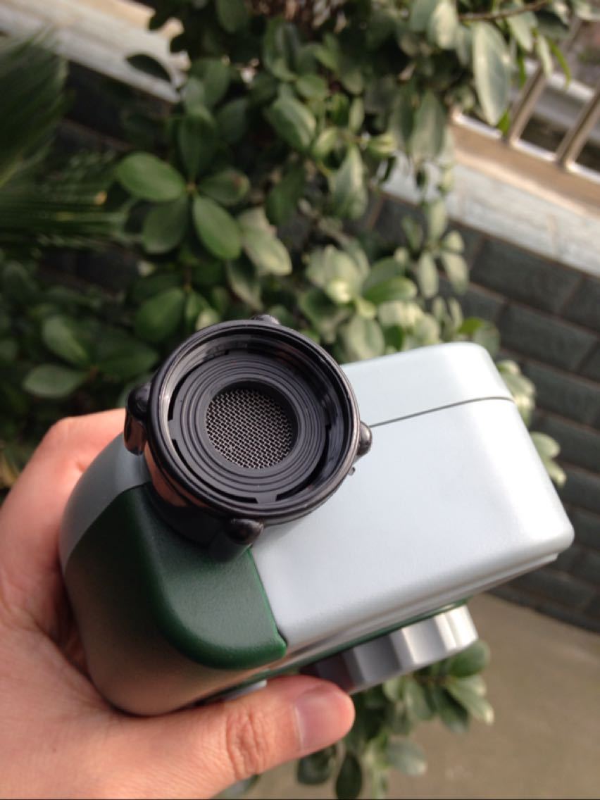 Hand holding a green and white device with a black circular component, outdoor setting