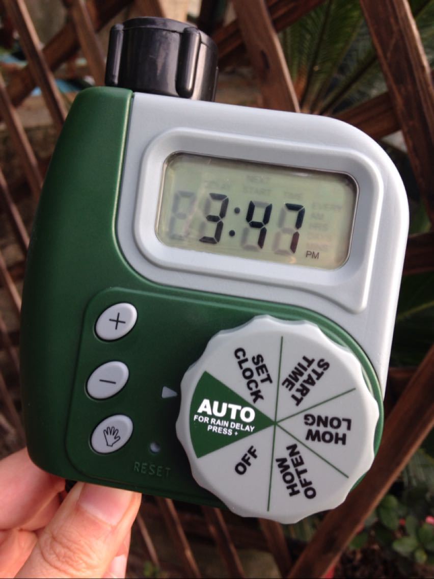 Digital timer with a green and white design held by a hand, with a blurred background.
