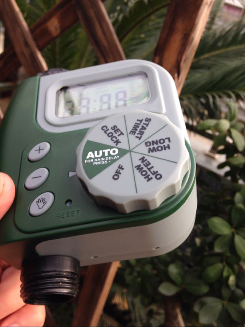 Garden timer with digital display held in hand, blurred greenery in the background