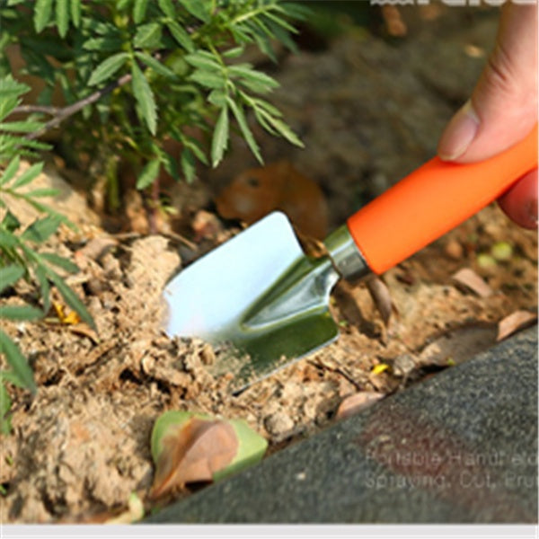 Person using a small gardening tool to dig into the soil near plants.