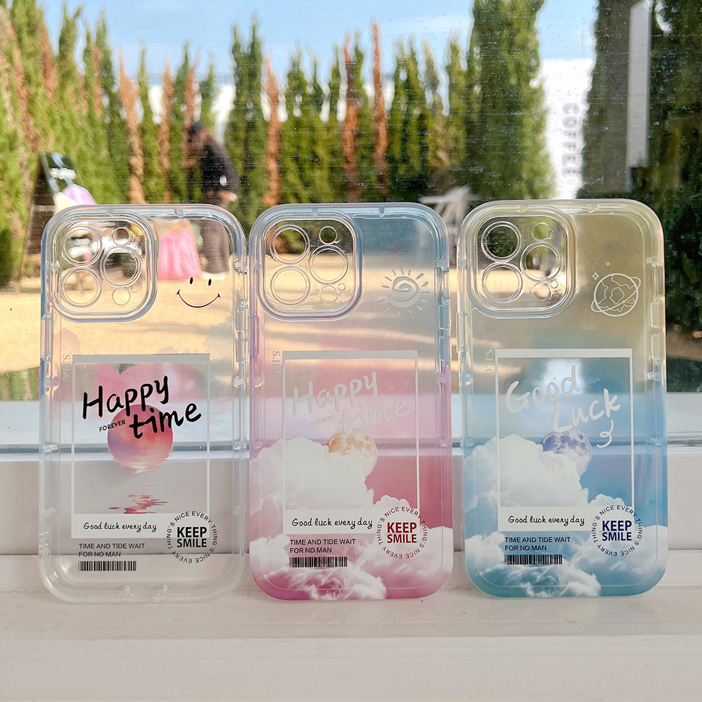 Three clear phone cases with printed designs and text on a reflective surface.
