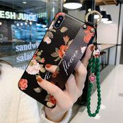 Hand holding a phone case with floral design and green beaded strap in an indoor setting.