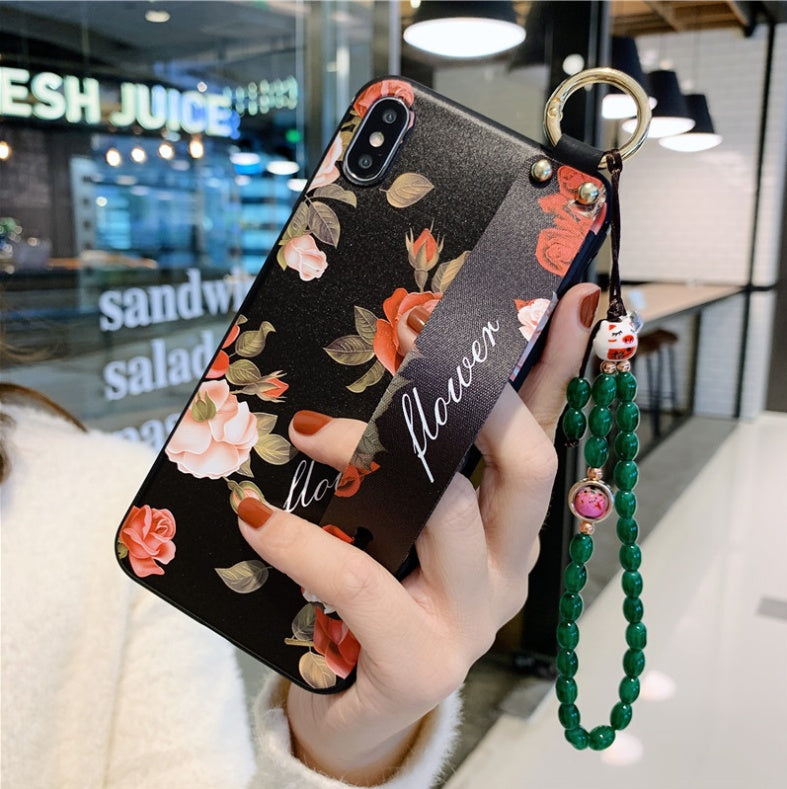 Hand holding a phone case with floral design and green beaded strap in an indoor setting.