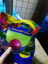 Packaged balloon ball with colorful packaging held by a hand against a tiled wall background.